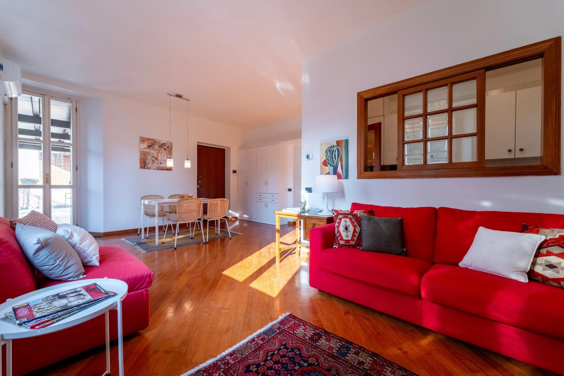 Una luminosa sala de estar y comedor con asientos rojos y una mesa junto a las ventanas.