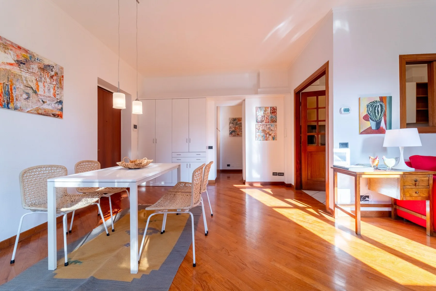 Un comedor luminoso con una mesa blanca, asientos tejidos y suelo de madera.