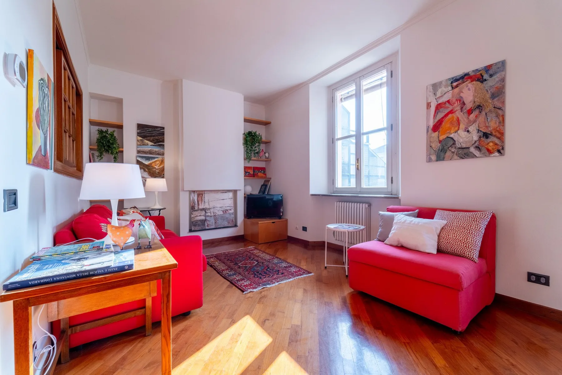 Una sala luminosa con asientos rojos, una mesa baja y una ventana grande.