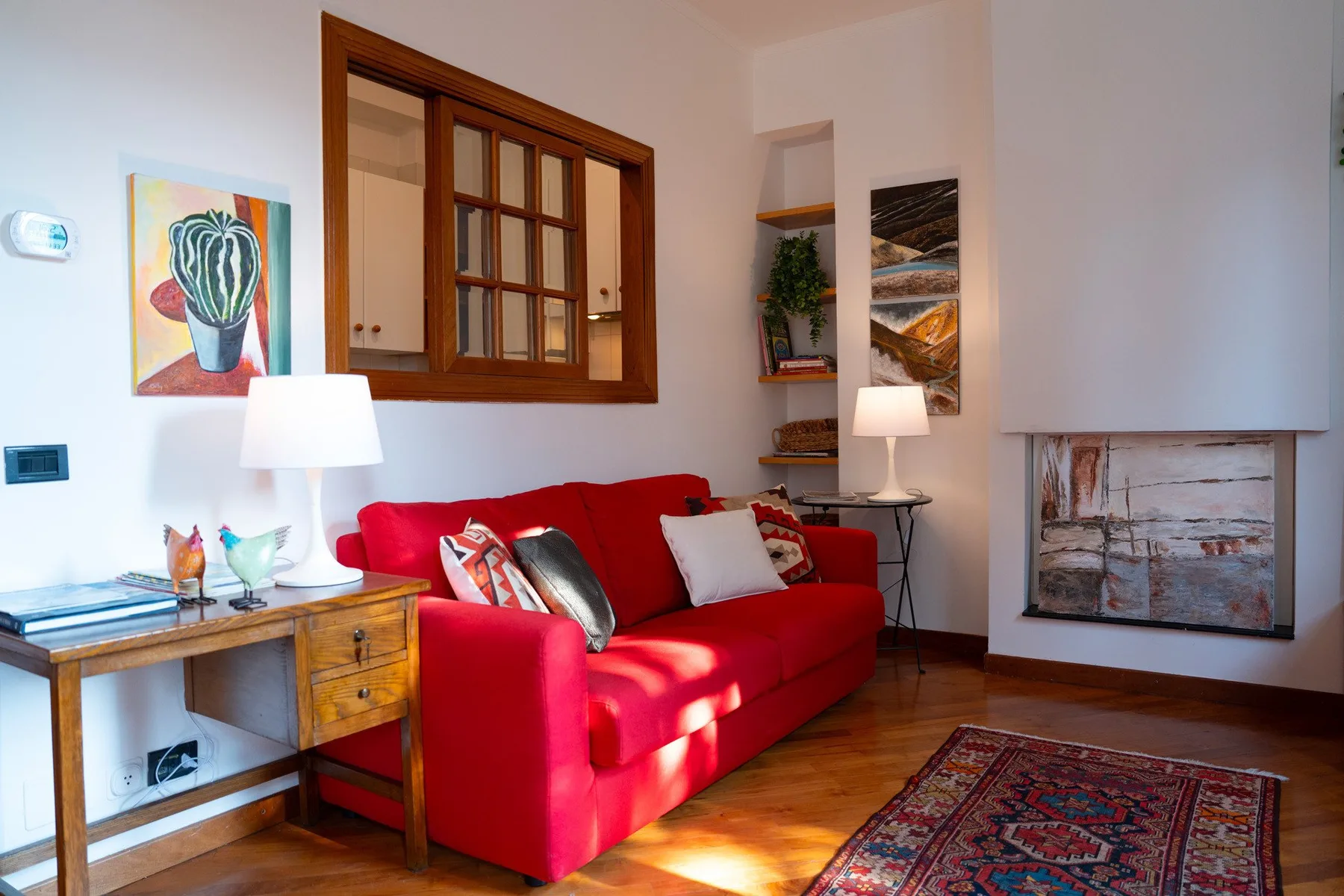 Una sala luminosa con asientos rojos, una mesa de madera y obras enmarcadas.