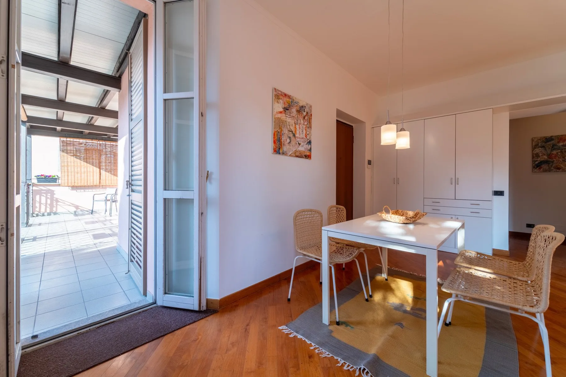 Comedor con una mesa blanca y sillas tejidas junto a una puerta de vidrio abierta.