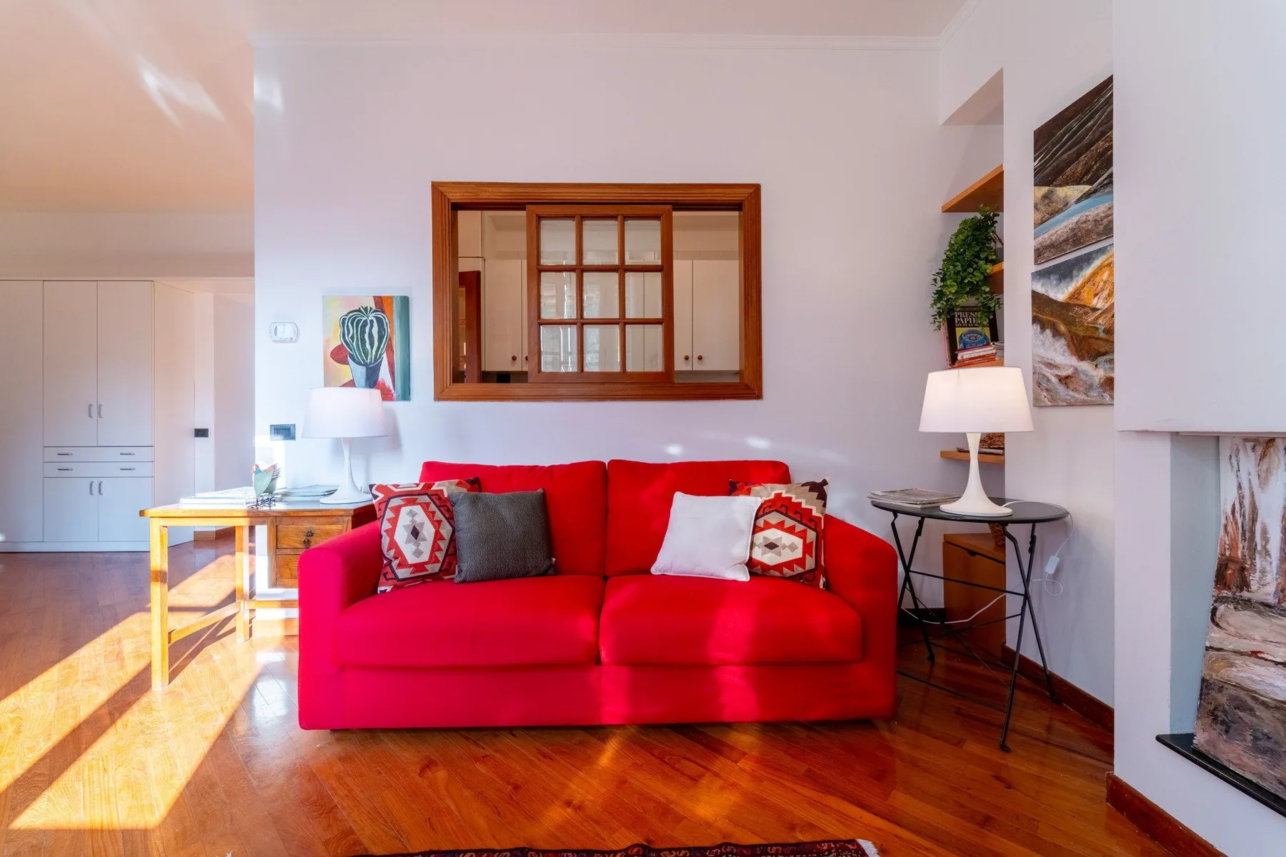 Una sala de estar con un sofá rojo, suelo de madera y cuadros en la pared.