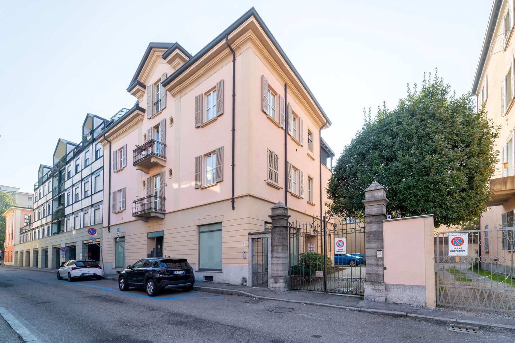 Un edificio rosado de varios pisos está en una calle urbana junto a una entrada con reja.