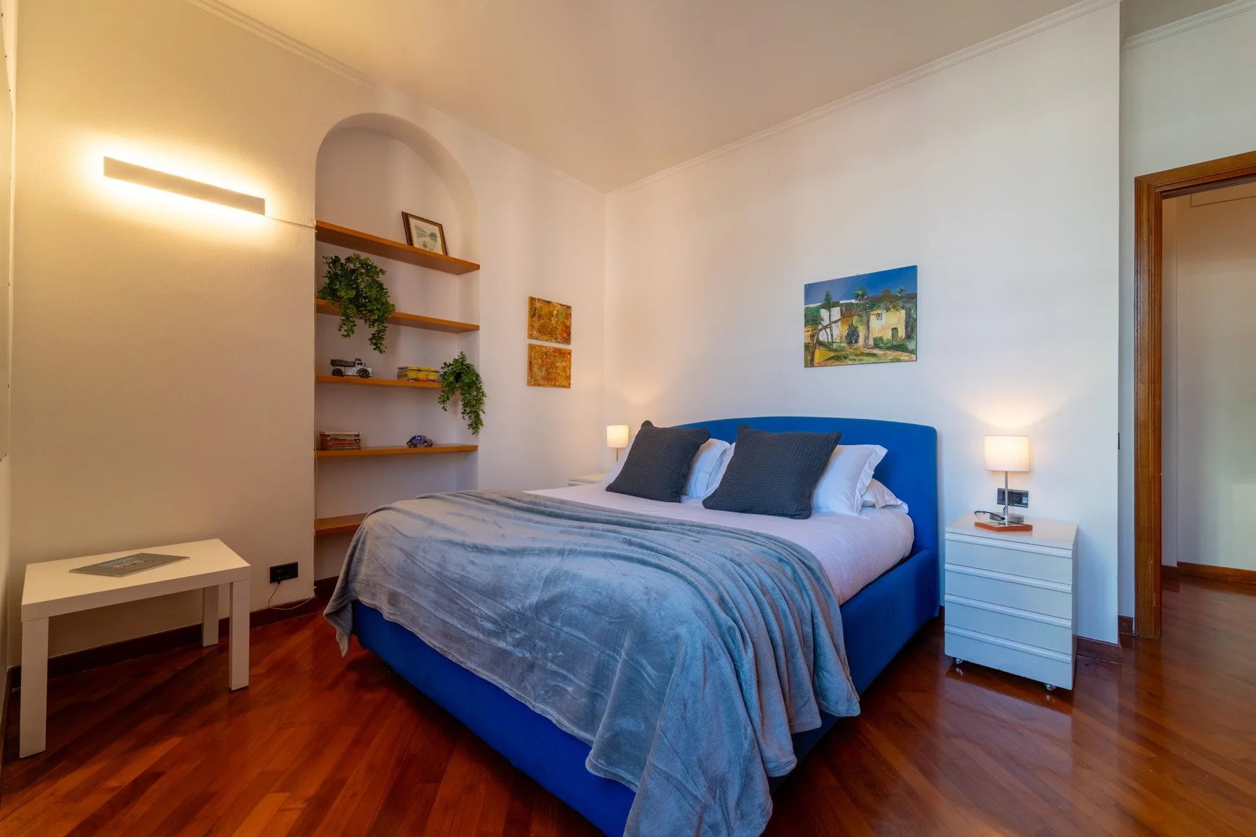 Un dormitorio con una cama azul, mesitas de noche y estantes empotrados.