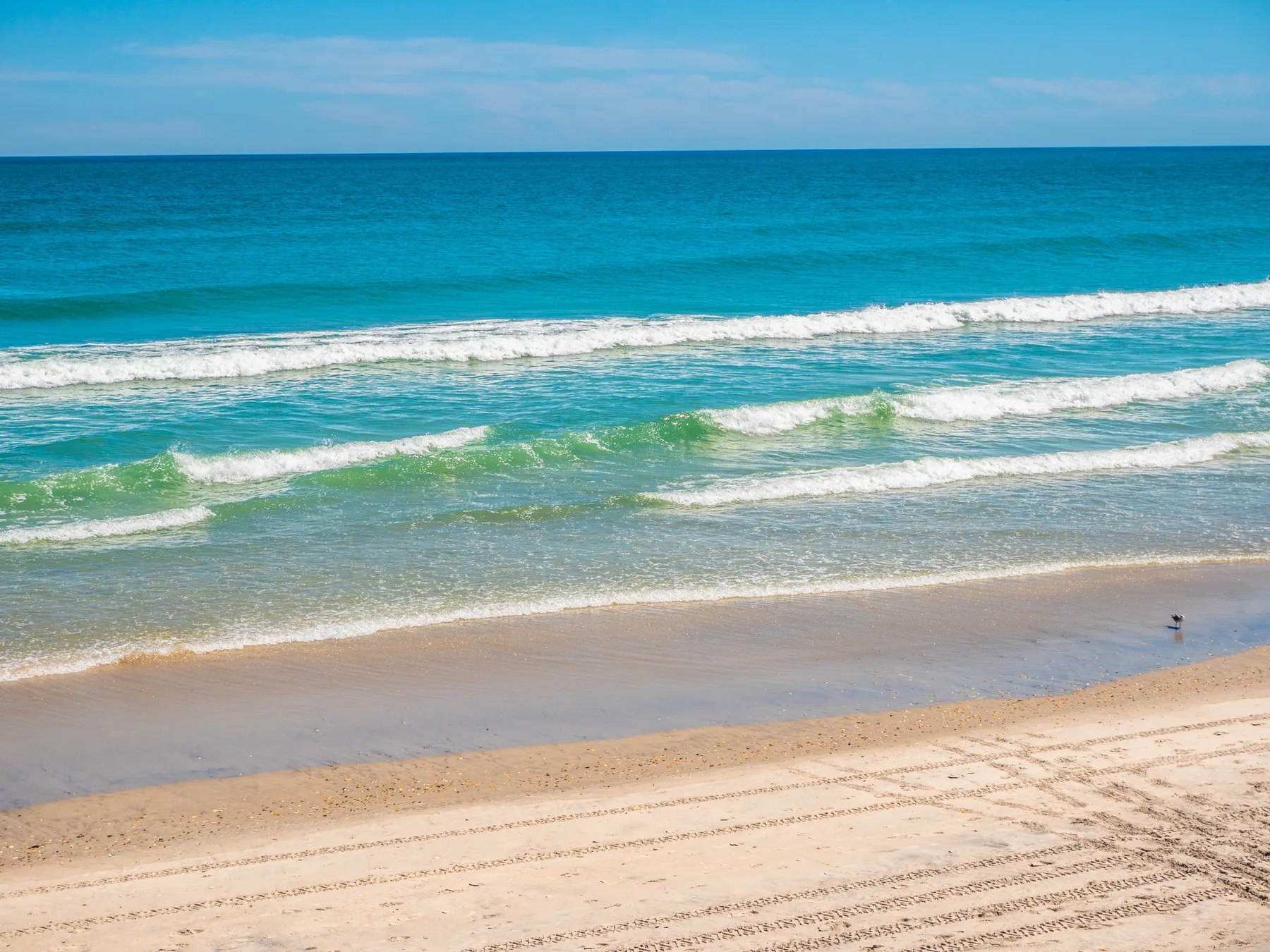 Una playa de arena se encuentra con aguas turquesas bajo un cielo azul despejado.