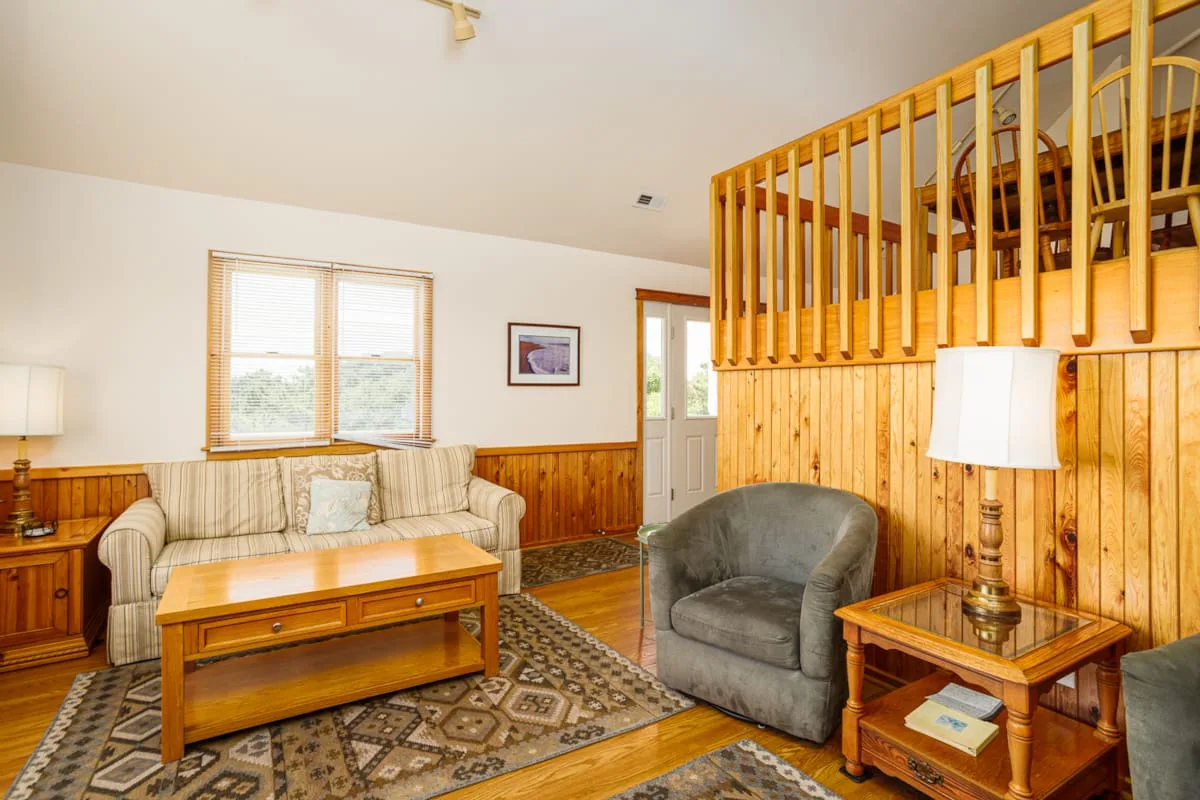 A living room with seating, a coffee table, and a wooden-railed loft.