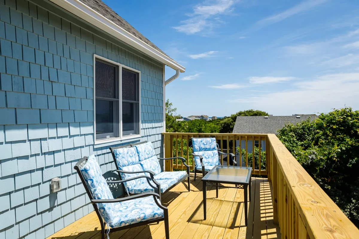 A sunny wooden deck with outdoor seating overlooks leafy surroundings.