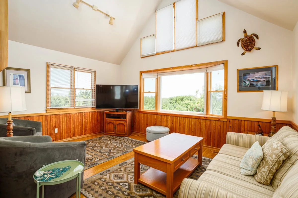 Una sala de estar con asientos, una mesa de centro y ventanas grandes.
