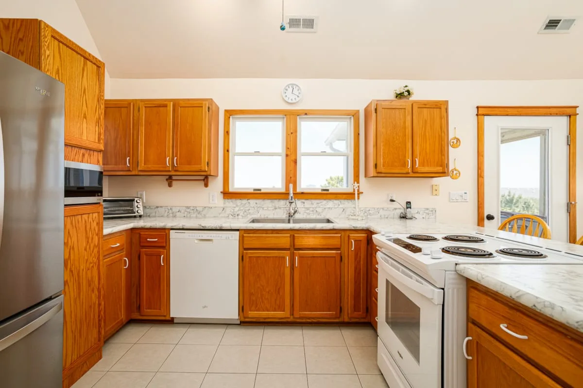 Una cocina con gabinetes de madera, piso de baldosas y una estufa.