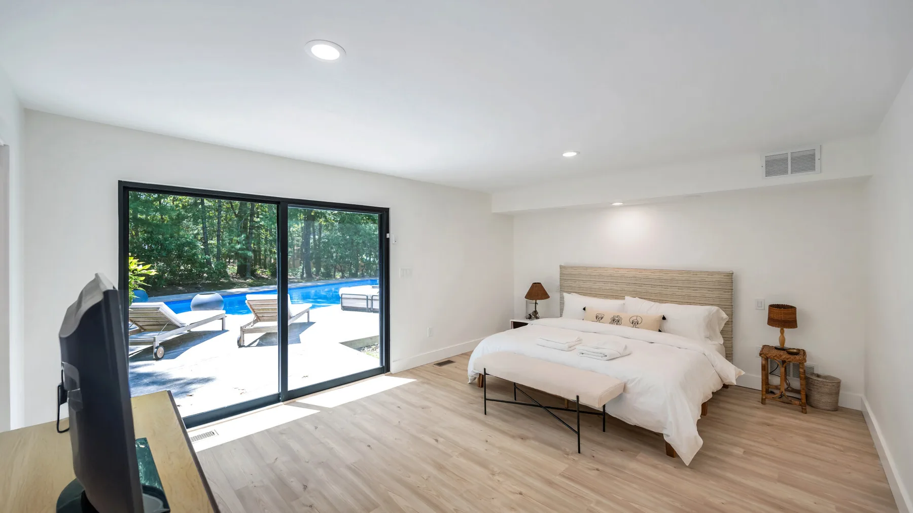 A bright bedroom with a bed beside large glass doors opening onto a pool area.