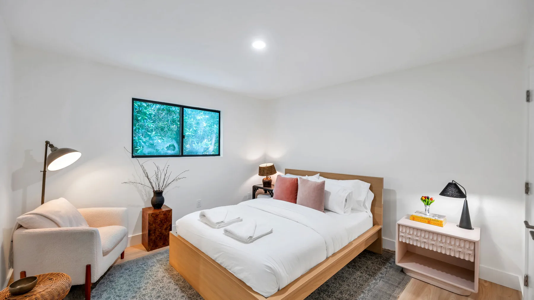 A bright bedroom with a made bed, bedside table, and window.
