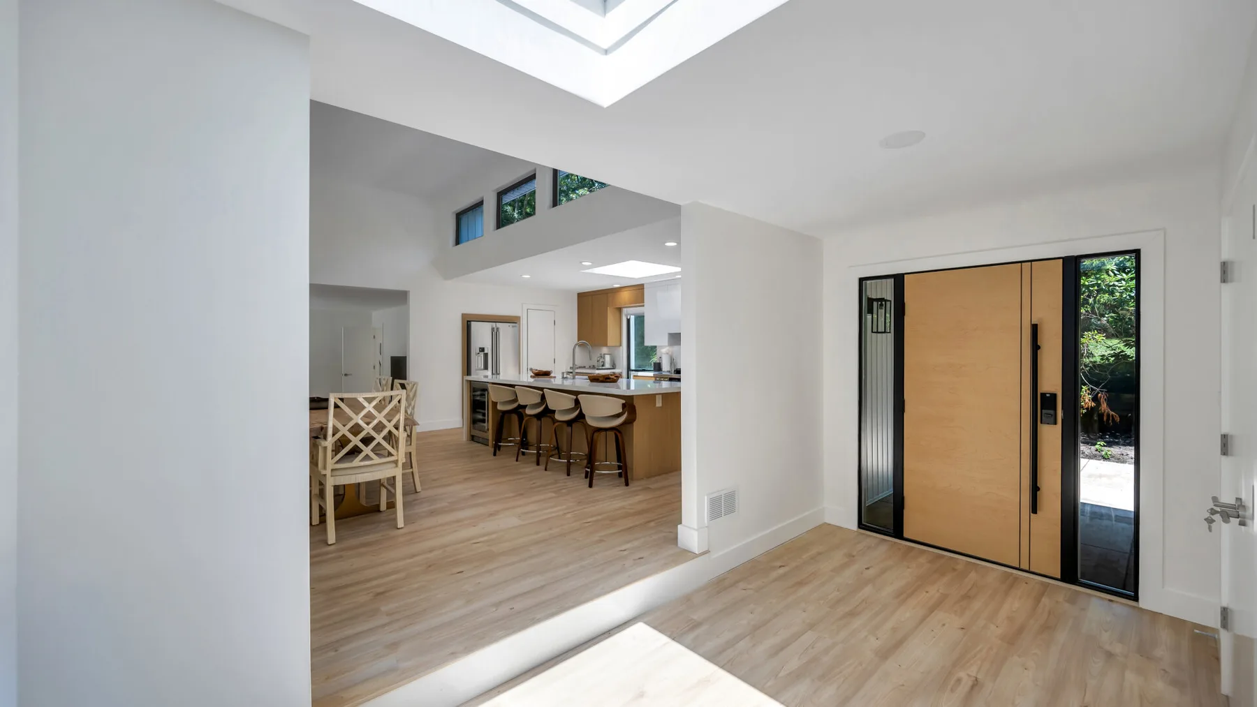 A bright entryway opens onto a kitchen and dining area with wood flooring.
