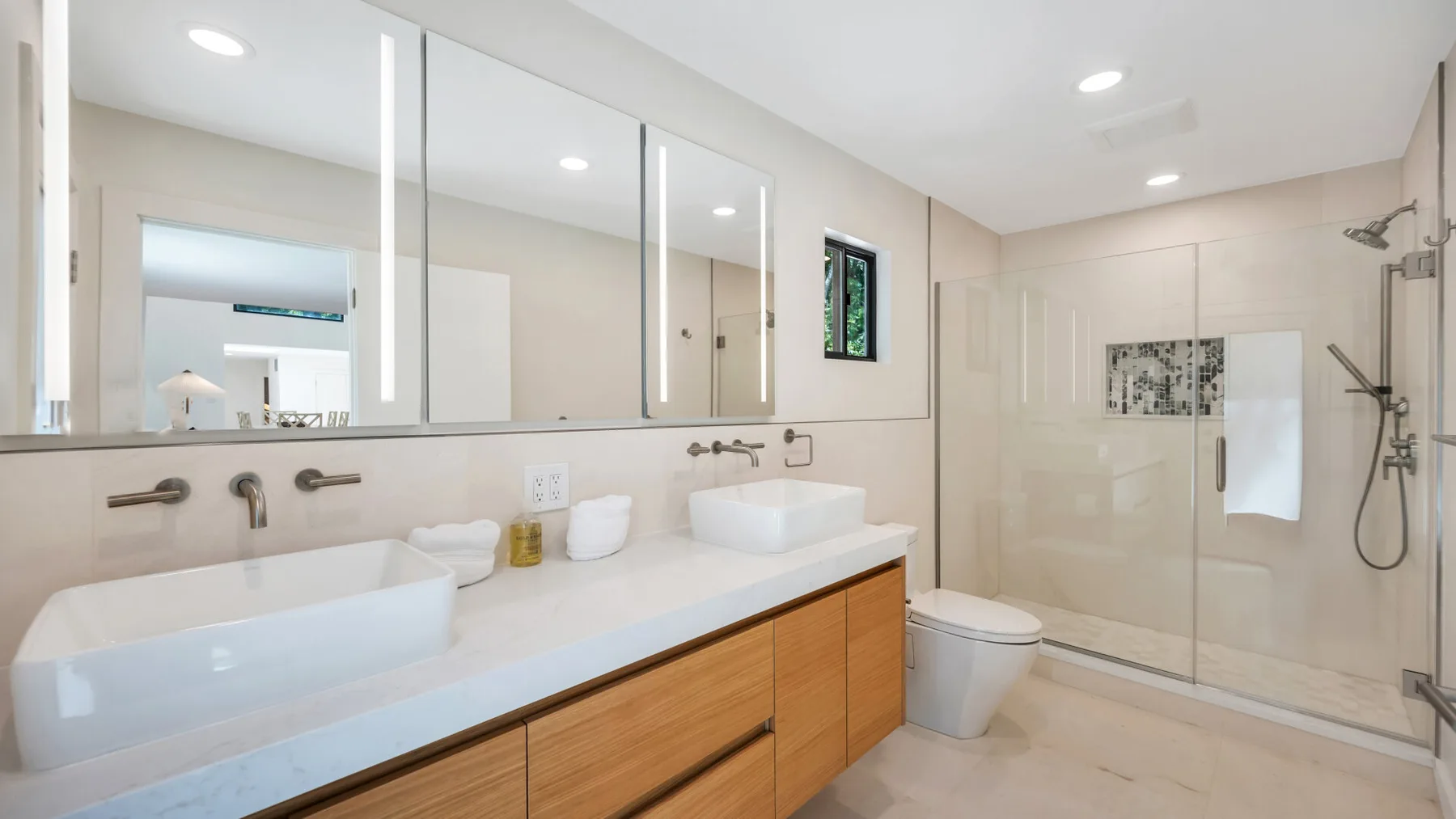A bright bathroom features a long vanity and a glass-enclosed shower.