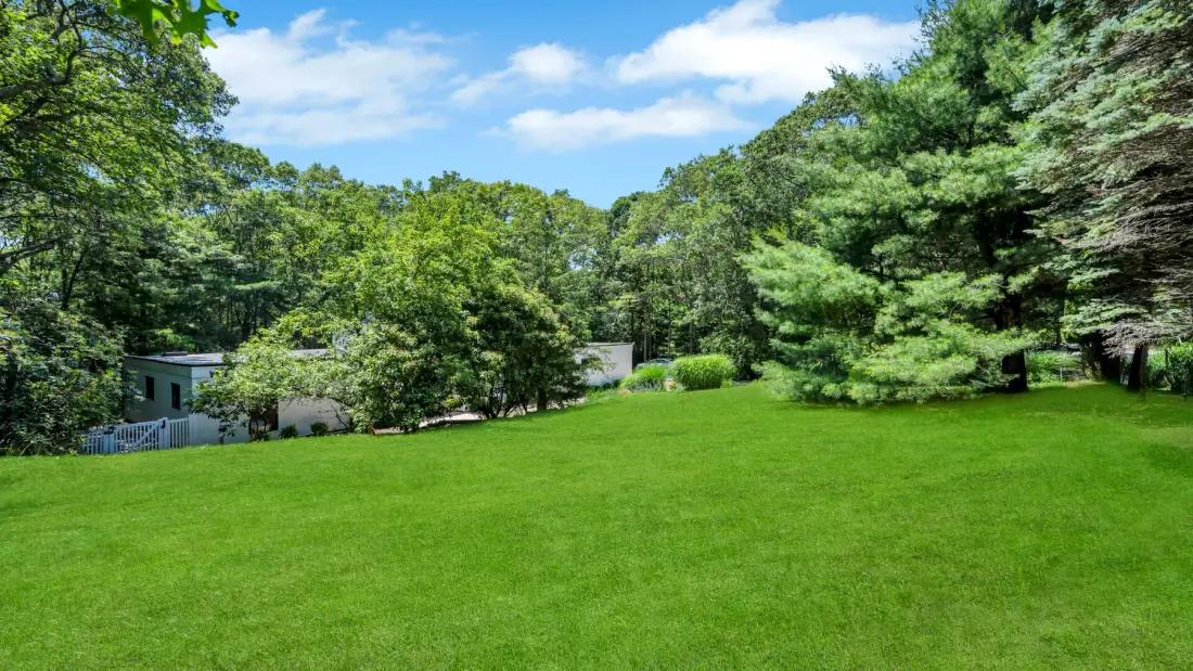 A broad green lawn stretches toward a tree-lined edge beneath a blue sky.