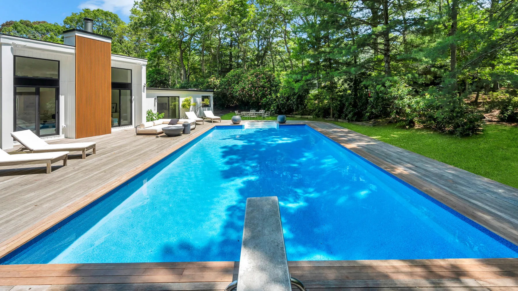 An outdoor swimming pool beside a modern house, with trees surrounding the garden.