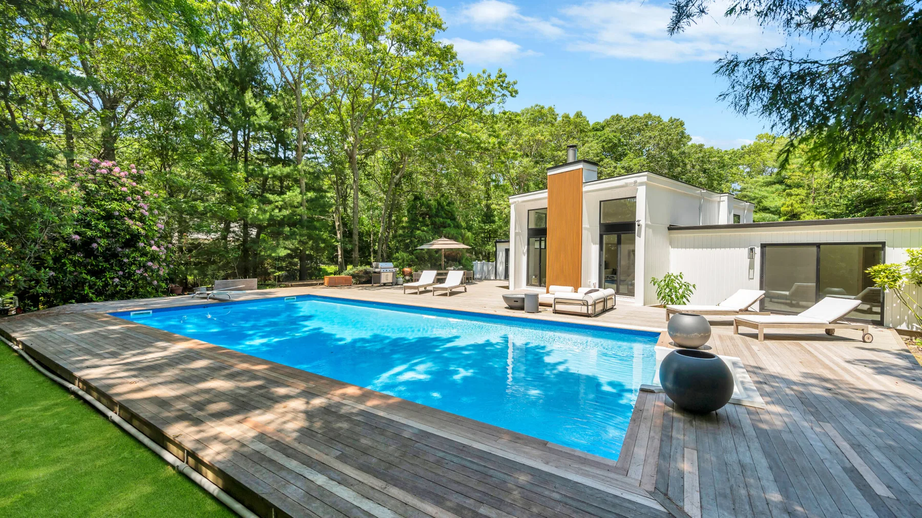An outdoor swimming pool beside a modern white house, surrounded by trees.