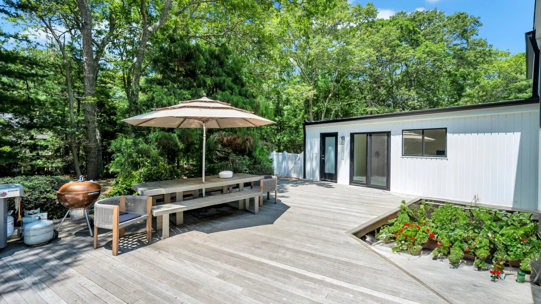 An outdoor deck with a picnic table and umbrella beside a white building.
