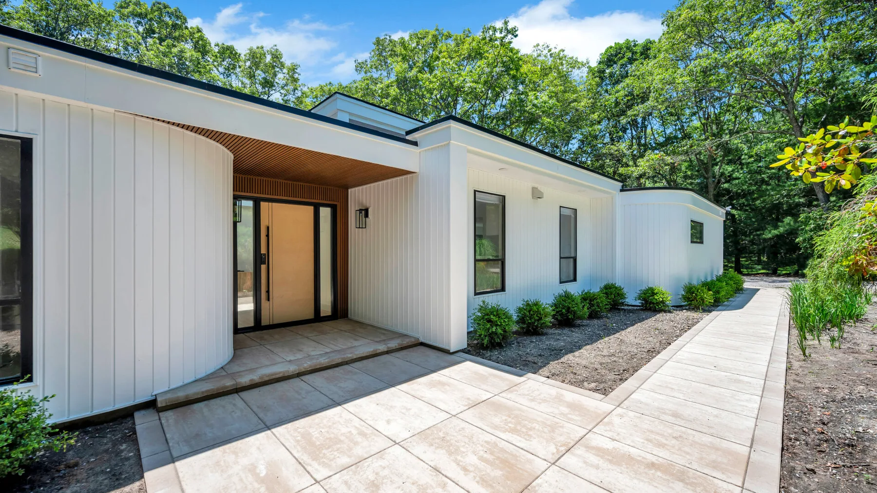 A modern white building with a paved walkway and leafy trees.