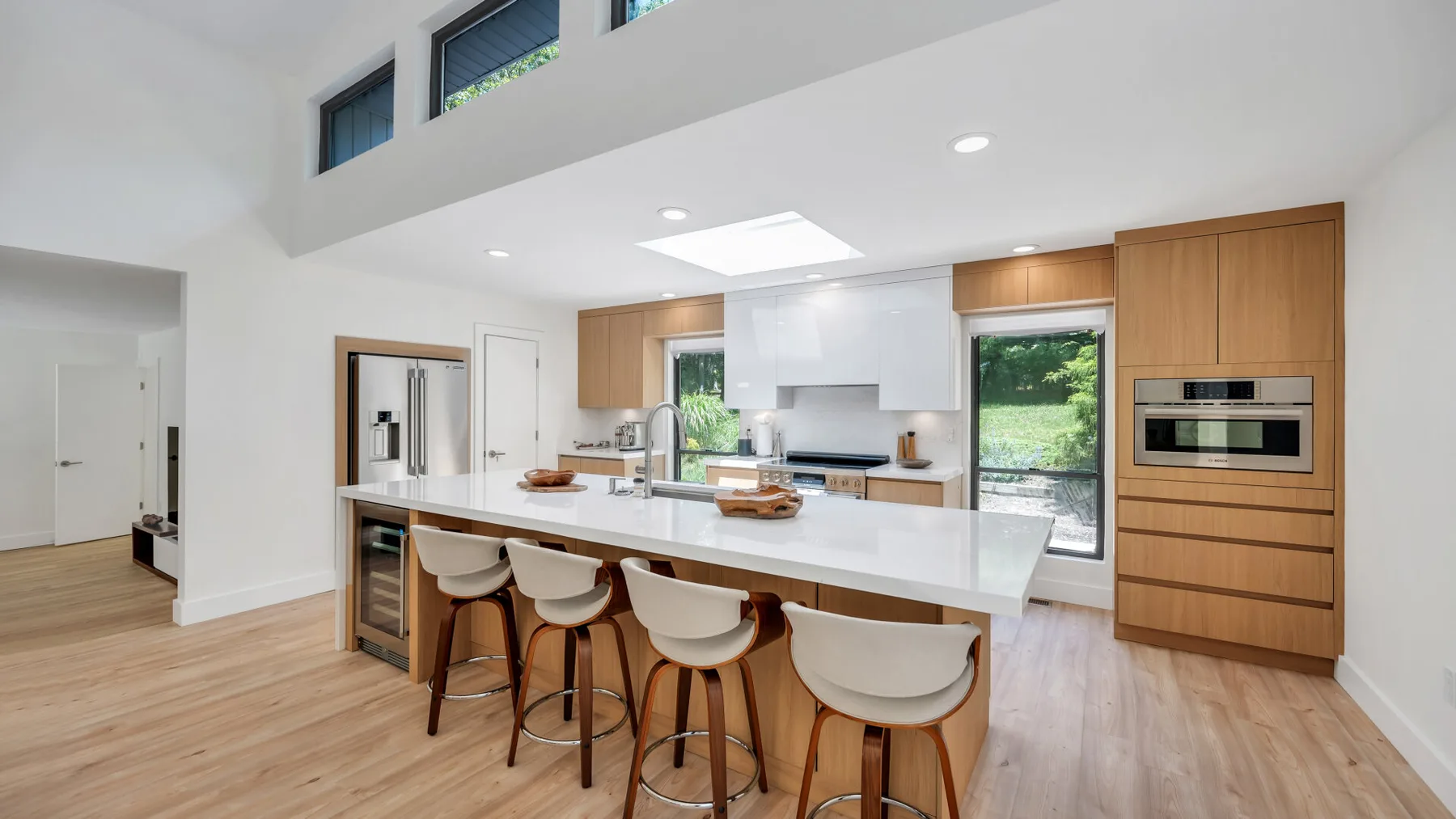 A bright kitchen with a long island and stools beneath a high ceiling.