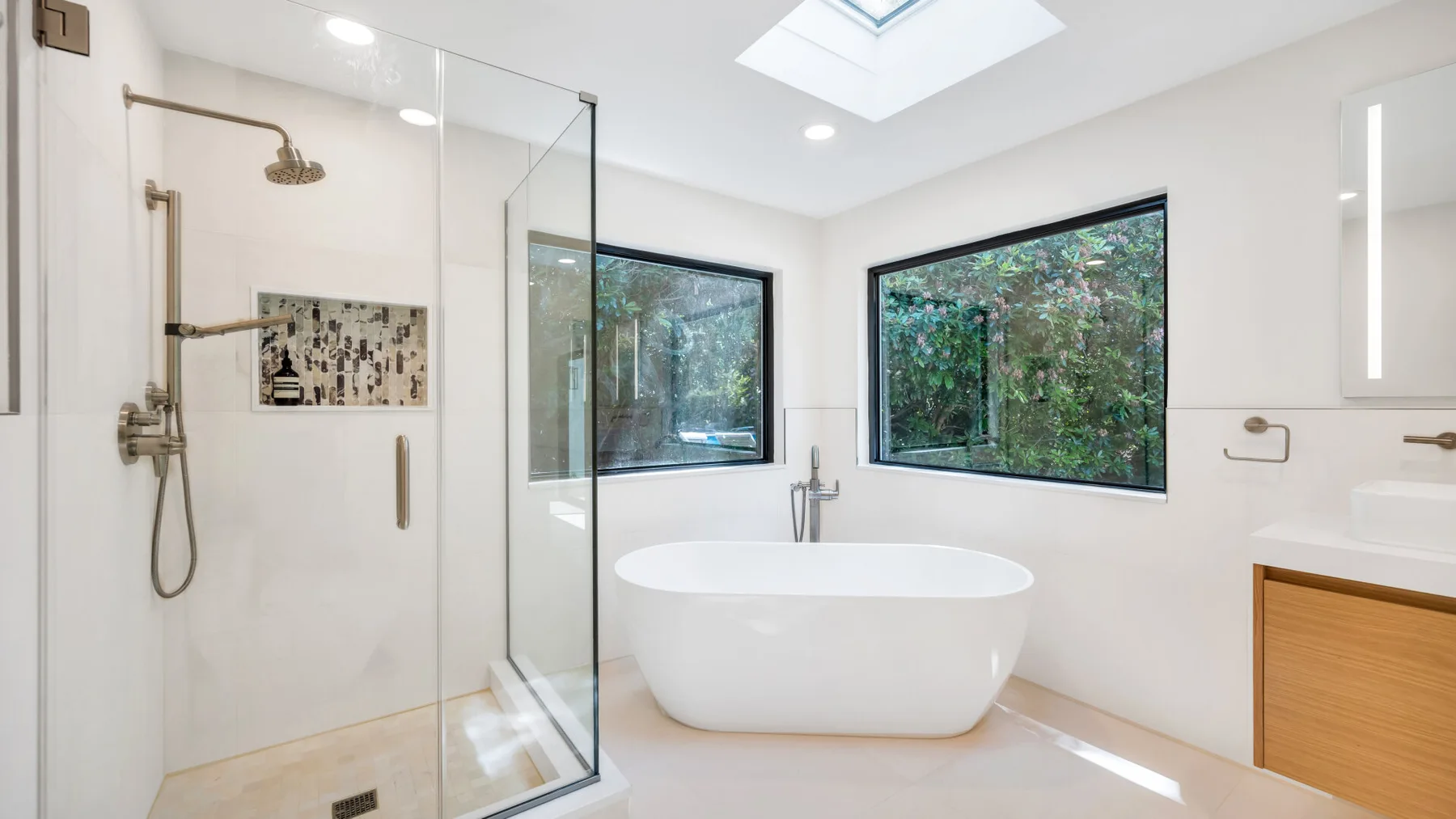 A bright bathroom with a freestanding bathtub, shower, and large windows.