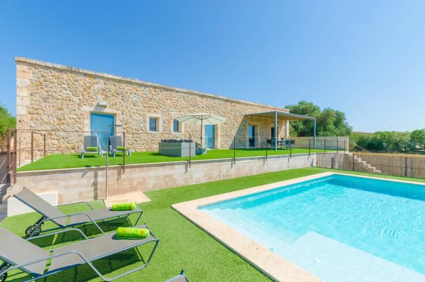 Una piscina al aire libre junto a un edificio de piedra y un patio con césped.