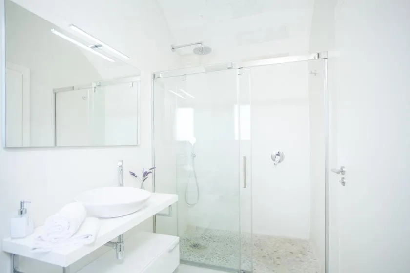 Un baño luminoso con una ducha de vidrio y un lavabo bajo un espejo.