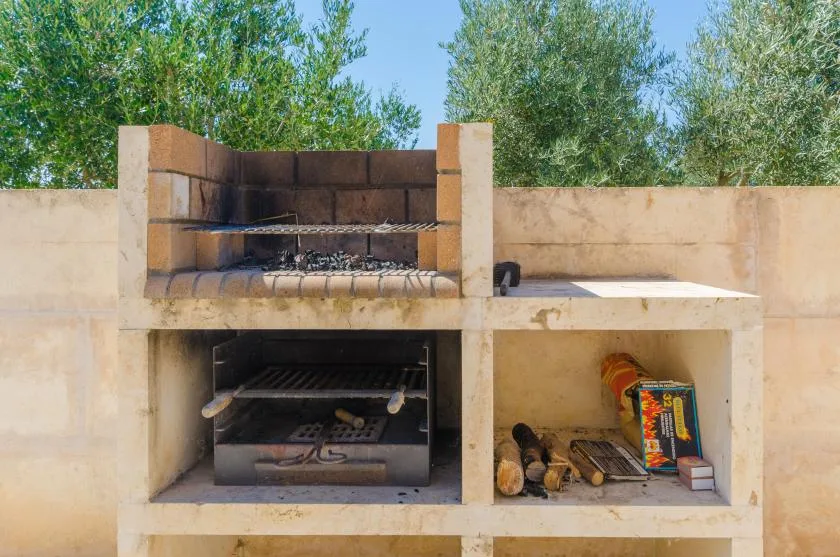 Una zona de barbacoa de obra al aire libre con una parrilla y un espacio para leña.