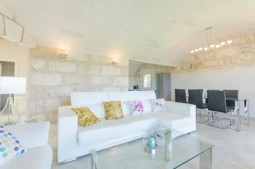 Una luminosa sala de estar y comedor con asientos blancos y una mesa de centro de vidrio.