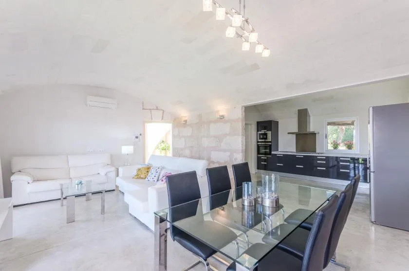 Una luminosa zona abierta de comedor y cocina con mesa de cristal y asientos blancos.
