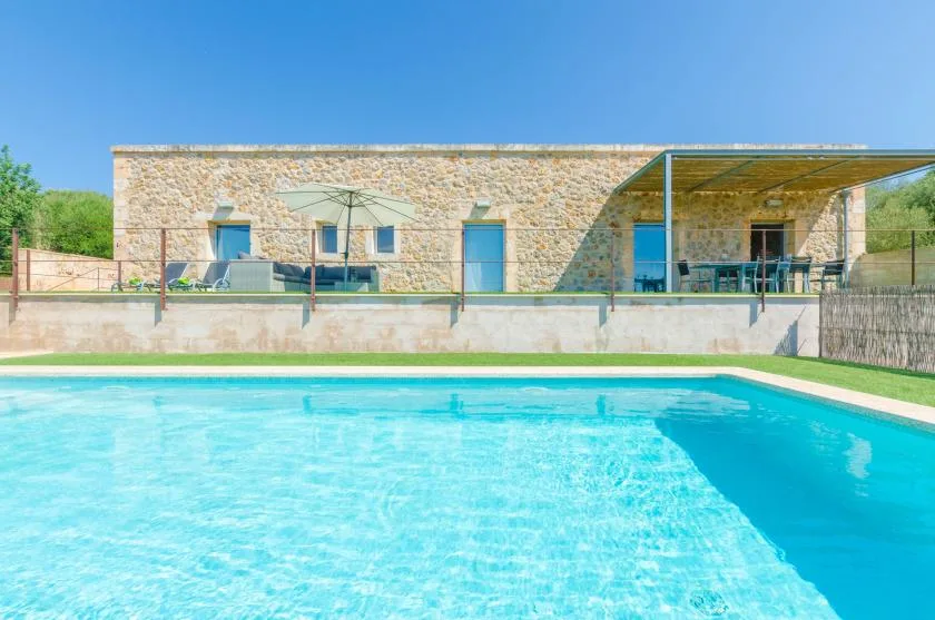 Una piscina está frente a un edificio de piedra con un patio cubierto.