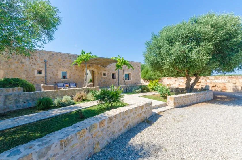 Un edificio de piedra está junto a un patio de grava con árboles y parterres.