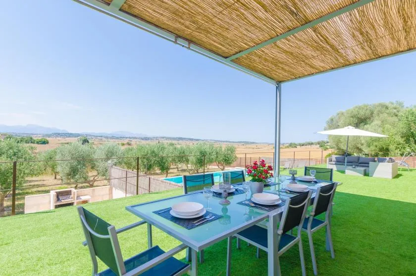 Una zona de comedor exterior bajo un toldo da a una piscina y al campo abierto.