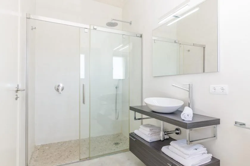 Un baño luminoso con una ducha de vidrio y un lavabo sobre un mueble oscuro.