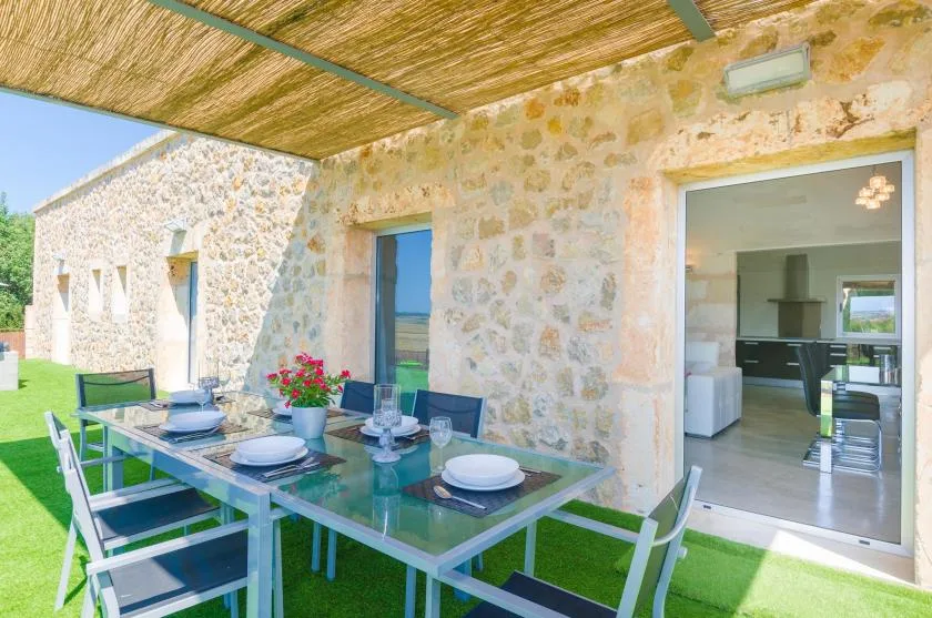 Comedor exterior cubierto con una mesa de vidrio junto a una casa de piedra.