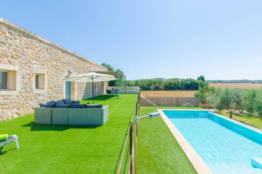 Una piscina junto a un edificio de piedra y una zona de estar al aire libre con césped.