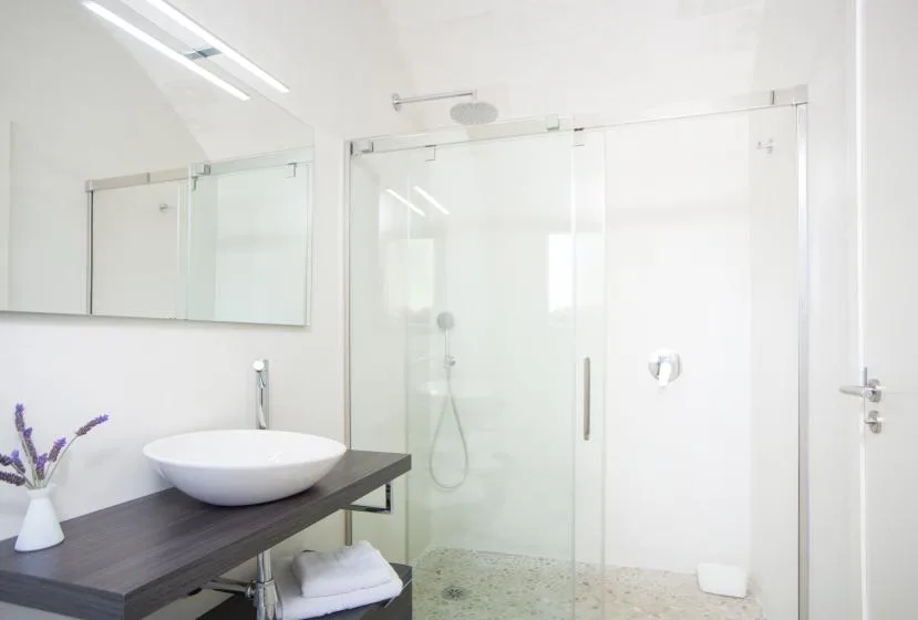 Un baño luminoso con una ducha de vidrio y un tocador oscuro con lavabo blanco.
