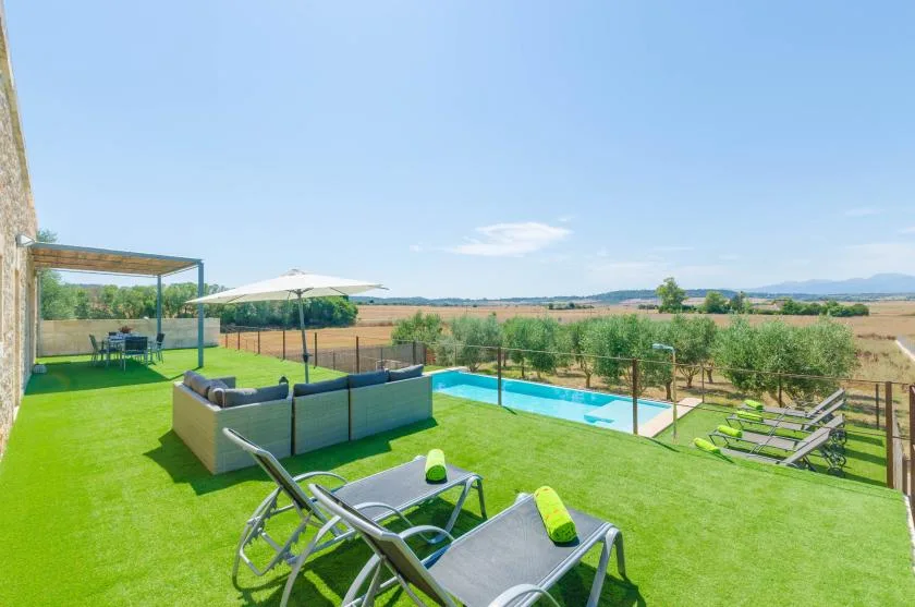 Patio exterior con asientos, una piscina y campo abierto al fondo.