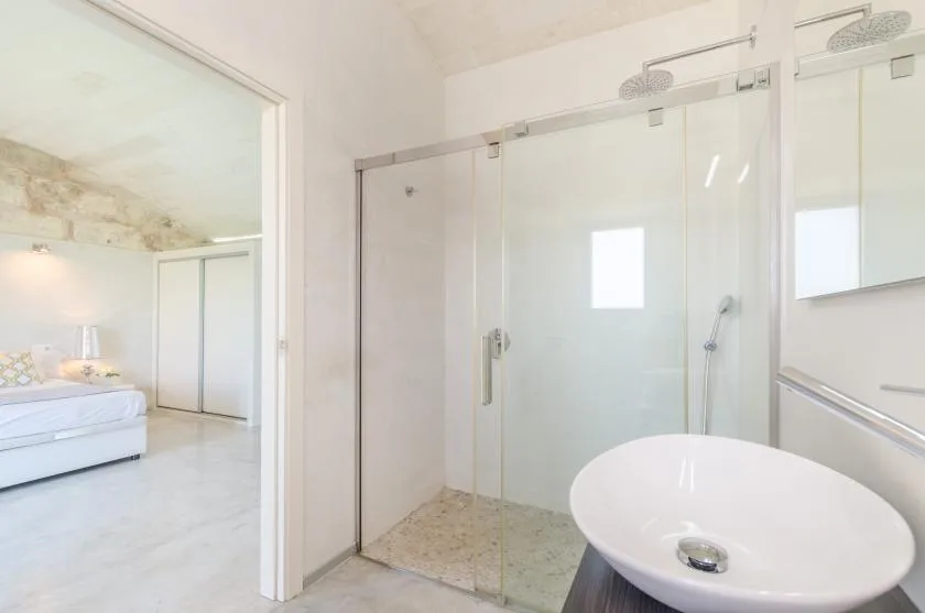 Un baño luminoso con una ducha de vidrio y un lavabo blanco sobre encimera.