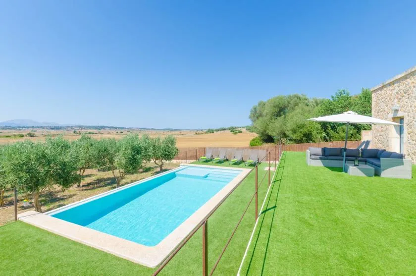 Una piscina al aire libre junto al césped, con el campo al fondo.