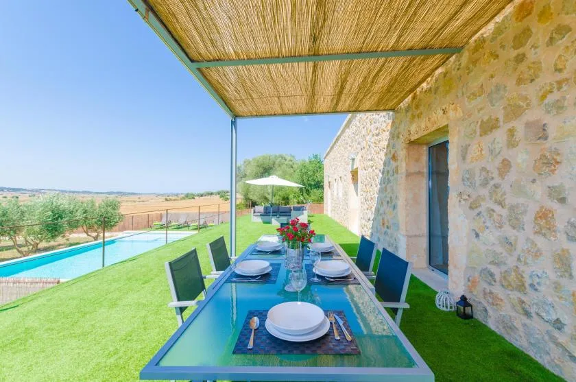Una mesa de comedor de vidrio está bajo un toldo tejido junto a un edificio de piedra.