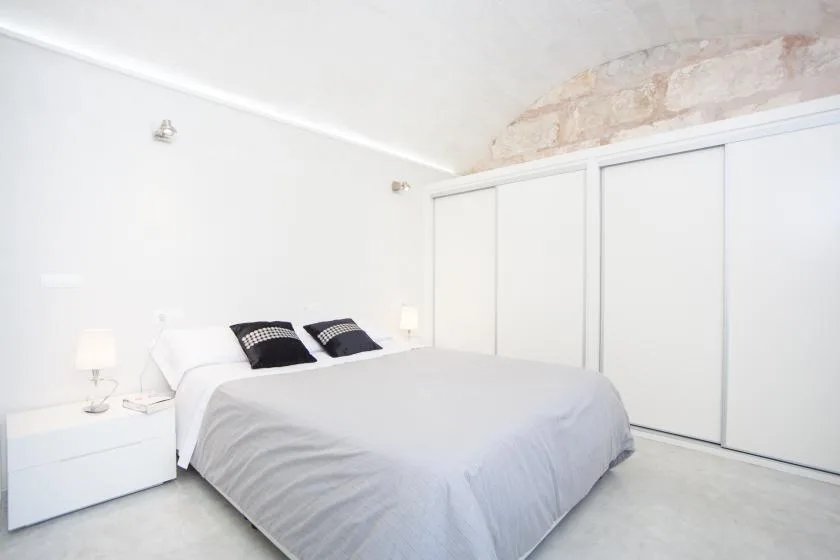Un dormitorio luminoso con una cama frente a puertas blancas de armario corredizas.
