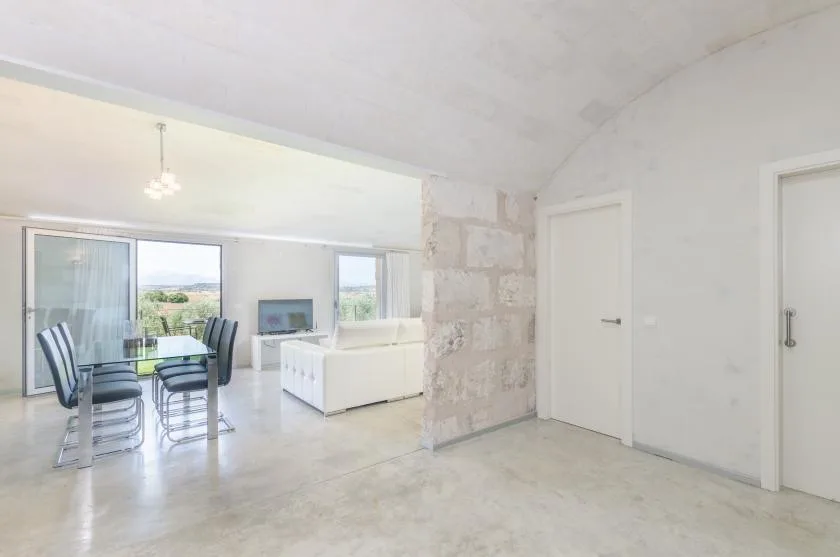 Una luminosa sala-comedor de planta abierta con una mesa de vidrio y asientos blancos.