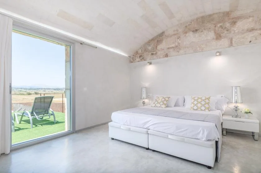 Un dormitorio luminoso con una cama grande junto a una puerta de cristal que da a una terraza.