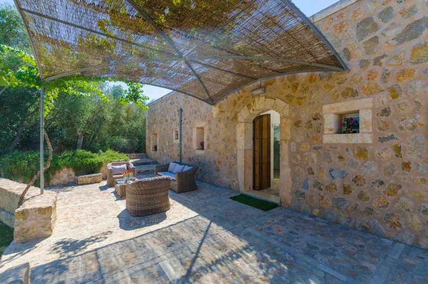 Un patio de piedra con asientos al aire libre está bajo una cubierta de sombra tejida.