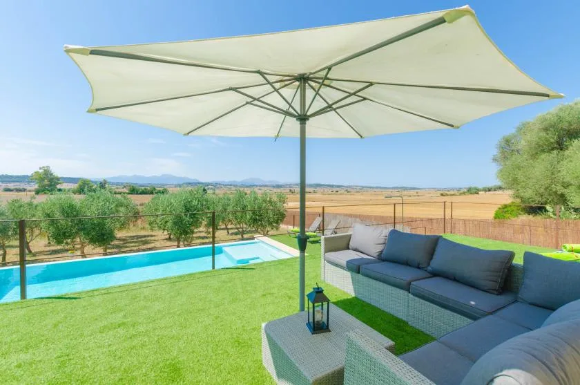 Asientos al aire libre junto a una piscina, bajo una gran sombrilla.