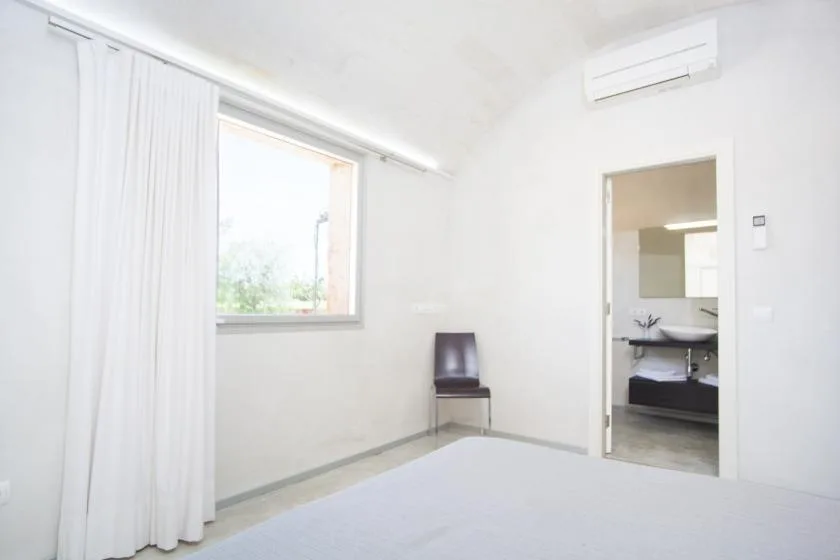 Una habitación luminosa con una ventana con cortinas y una puerta abierta al baño.