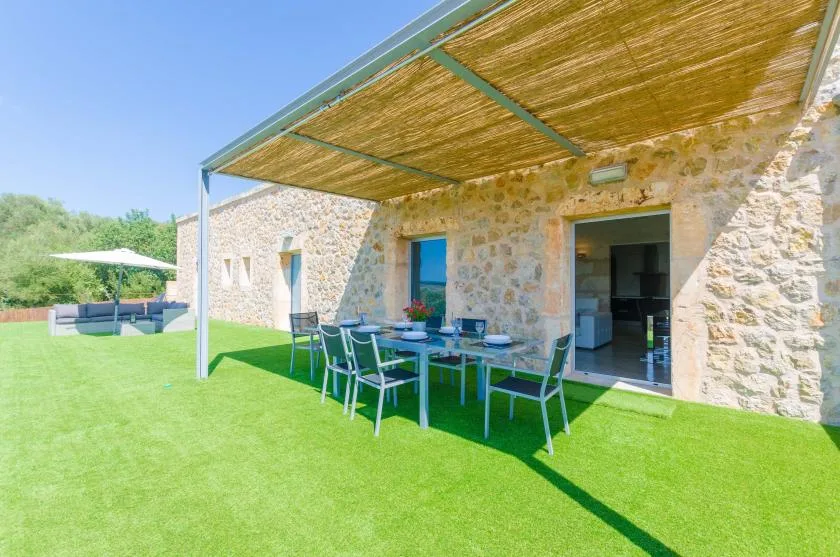 Patio de una casa de piedra con asientos para comer al aire libre bajo una pérgola.