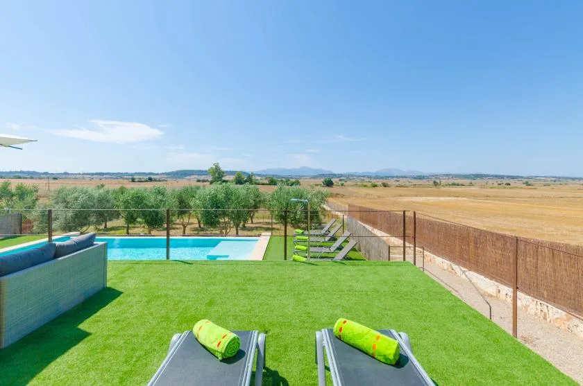 Una piscina al aire libre junto a un césped verde, con campos abiertos al fondo.