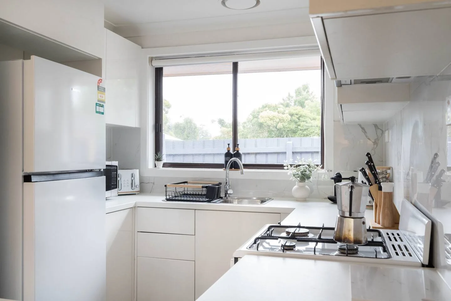 Una cocina luminosa con armarios blancos y una ventana grande sobre el fregadero.