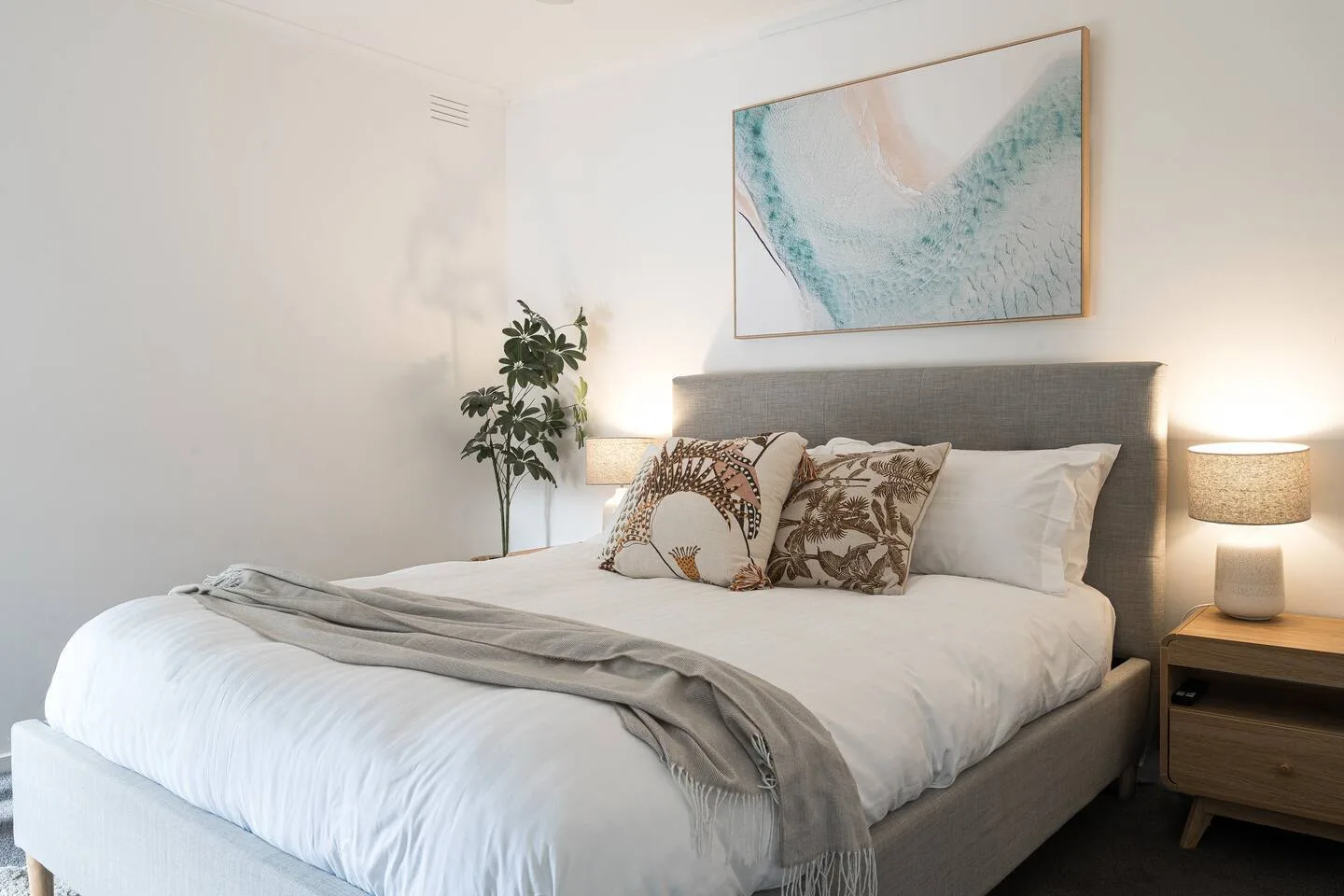 Un dormitorio con una cama bien tendida, cojines decorativos y un cuadro sobre el cabecero.
